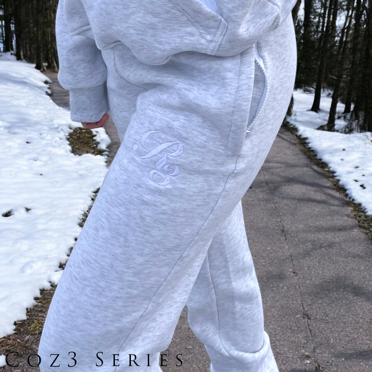 A close-up of a person wearing gray Coz3 Max Unisex Sweatpants, showing the side pocket and the brand's logo on the leg of the pants.